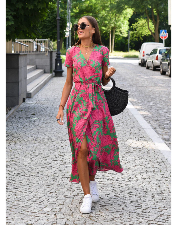 Eine Frau trägt ein rot-grünes Sommerkleid, dazu weiße Schuhe und eine schwarze Handtasche